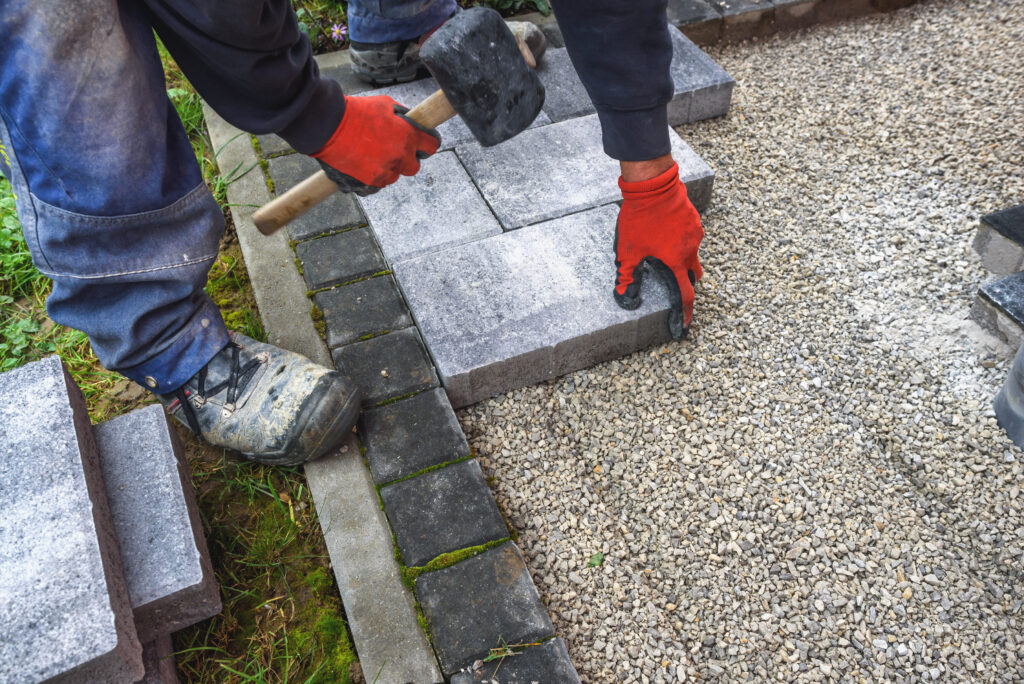 Worker wearing red gloves laying grey concrete pavers on a gravel path